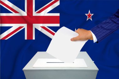 Ülkedeki seçimler - oy sandığında oy kullanma. Bir adam oyunu sandığa koyuyor. Arkaplanda Yeni Zelanda Bayrağı.