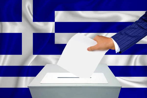 Elections in the country - voting at the ballot box. A man's hand puts his vote into the ballot box. Flag Greece on background.