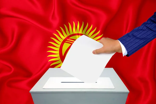 Elections in the country - voting at the ballot box. A man\'s hand puts his vote into the ballot box. Flag Kyrgyzstan on background.