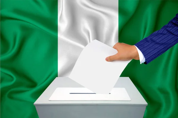 Elections in the country - voting at the ballot box. A man\'s hand puts his vote into the ballot box. Flag Nigeria on background.