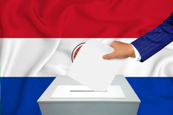 Elections in the country - voting at the ballot box. A man\'s hand puts his vote into the ballot box. Flag Paraguai on background.