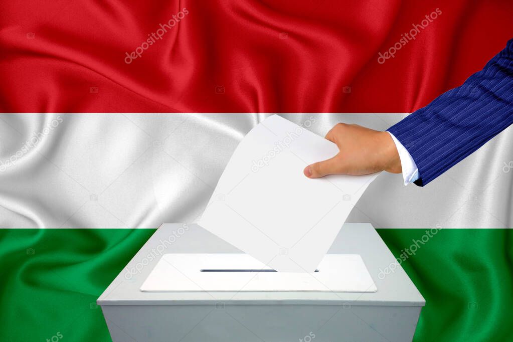 Elections in the country - voting at the ballot box. A man's hand puts his vote into the ballot box. Flag Hungary on background.