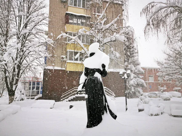 Snow-covered trees, bushes, a statue in the city. Russia, Belorechensk, winter city. Snow-covered sculpture.