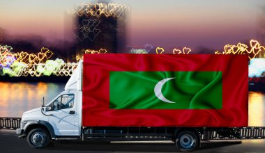 Bulanık bir şehir ve nehrin arka planına karşı beyaz bir minibüsün yanında Maldivler bayrağı. Lojistik kavramı