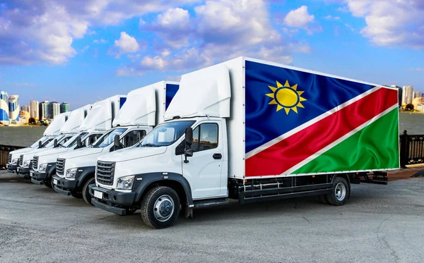 Namibia flag on the back of Five new white trucks against the backdrop of the river and the city. Truck, transport, freight transport. Freight and Logistics Concept