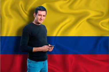 Arka planda Kolombiya bayrağı var. Genç adam gülümsüyor ve elinde bir akıllı telefon tutuyor. Tasarım çözümleri kavramı.