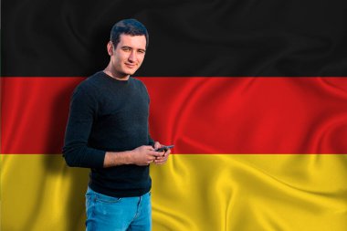 Arkaplanda Almanya bayrağı var. Genç adam gülümsüyor ve elinde bir akıllı telefon tutuyor. Tasarım çözümleri kavramı.