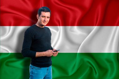 Dokunun arka planında Macaristan bayrağı var. Genç adam gülümsüyor ve elinde bir akıllı telefon tutuyor. Tasarım çözümleri kavramı.