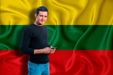 Arka planda Litvanya bayrağı var. Genç adam gülümsüyor ve elinde bir akıllı telefon tutuyor. Tasarım çözümleri kavramı.