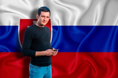 Arka planda Slovakya bayrağı var. Genç adam gülümsüyor ve elinde bir akıllı telefon tutuyor. Tasarım çözümleri kavramı.