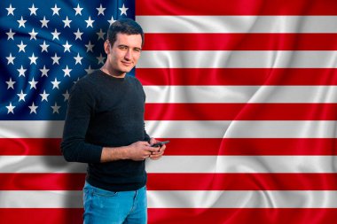 Arka planda Amerikan bayrağı var. Genç adam gülümsüyor ve elinde bir akıllı telefon tutuyor. Tasarım çözümleri kavramı.