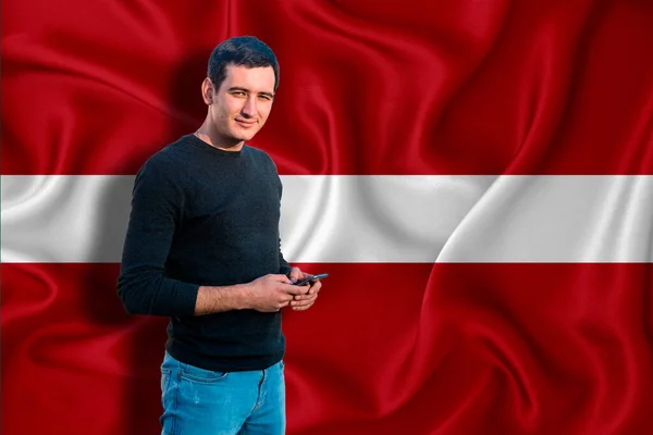 Latvia flag on the background of the texture. The young man smiles and holds a smartphone in his hand. The concept of design solutions.