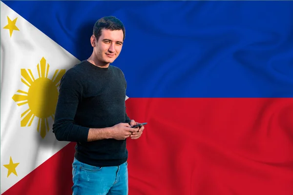 Philippines flag on the background of the texture. The young man smiles and holds a smartphone in his hand. The concept of design solutions.