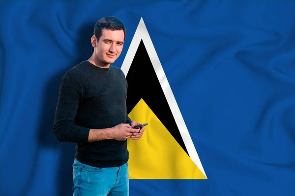Saint Lucia flag on the background of the texture. The young man smiles and holds a smartphone in his hand. The concept of design solutions.
