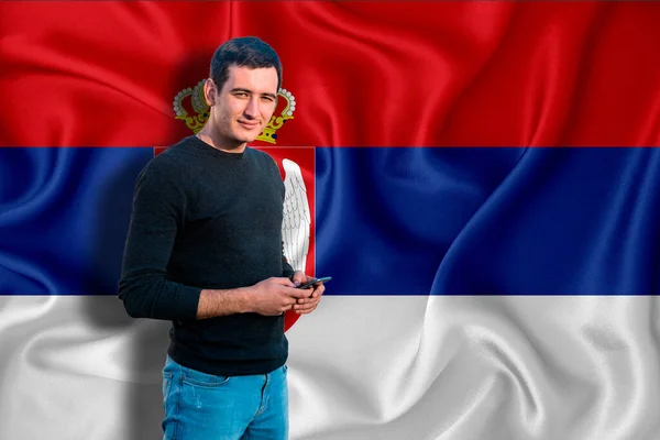 Serbian flag on the background of the texture. The young man smiles and holds a smartphone in his hand. The concept of design solutions.