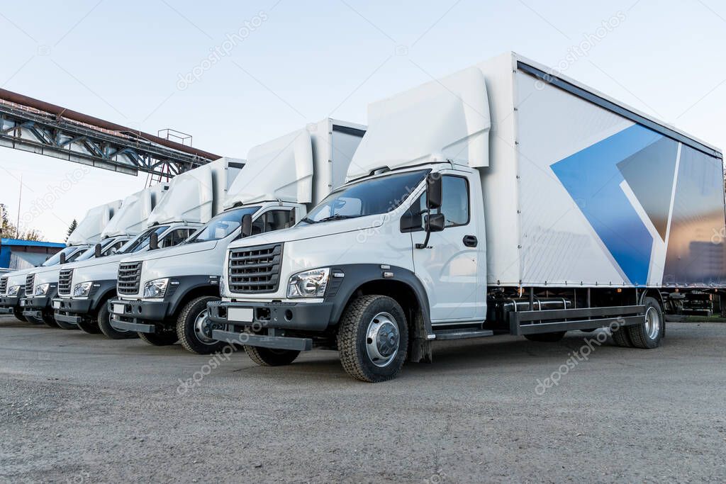 Five new white trucks ready for departure are parked. Delivery or shipment of goods in a conceptual manner.