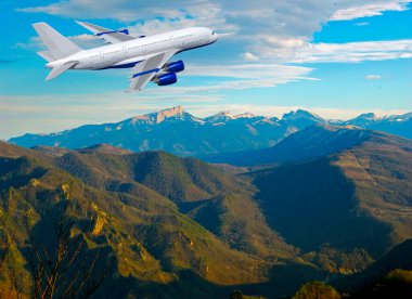 Ticari beyaz uçak dramatik bulutların ve dağların üzerinde uçuyor. Seyahat kavramı.