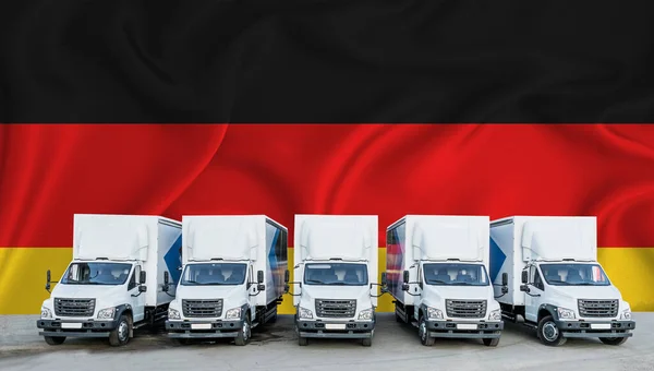 背景中的德国国旗 五辆新的白色卡车停在停车场 货物运输 运费和物流概念 — 图库照片