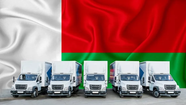 stock image Madagascar flag in the background. Five new white trucks are parked in the parking lot. Truck, transport, freight transport. Freight and logistics concept