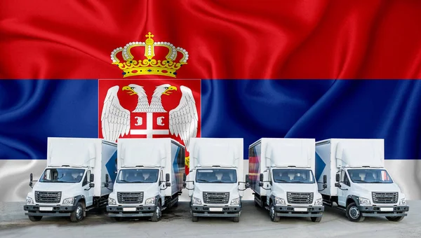 Serbian flag in the background. Five new white trucks are parked in the parking lot. Truck, transport, freight transport. Freight and logistics concept