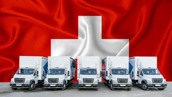 Switzerland flag in the background. Five new white trucks are parked in the parking lot. Truck, transport, freight transport. Freight and logistics concept