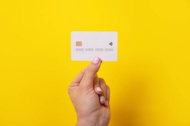 Elinde kredi kartı, sarı arka planda elektronik çip var.