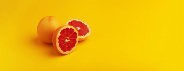 Whole and sliced grapefruit over yellow background, panoramic image
