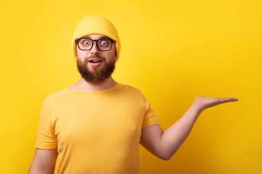 Yakışıklı beyaz adam sarı arka planda elini boş gösteriyor.