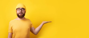 Yakışıklı beyaz adam sarı arkaplan üzerinde eli boş geziyor. Yazmak için yeri olan panoramik bir düzen.