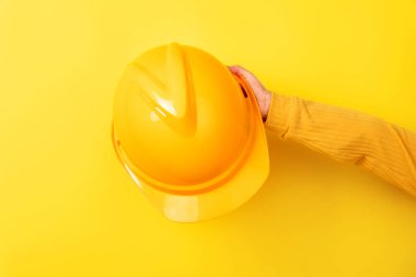 Sarı arka plana karşı sarı bir kaskı tutmak, inşaat, güvenlik ve takım çalışmasını sembolize ediyor..