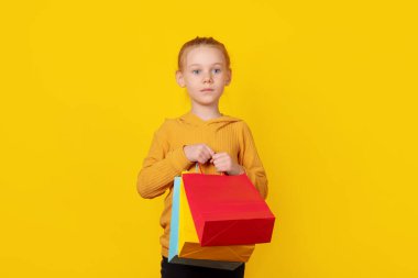 Parlak sarı arka planda renkli alışveriş torbaları taşıyan genç bir kız. Perakende, satış ya da yaşam tarzı kavramları için mükemmel..