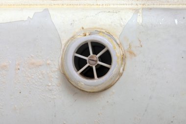 Eski, lekeli bir küvet giderine yakın çekim, beyaz diş minesi ve görünür kirlilik, bakım ve temizlik için aşınma izleri gösteriyor..