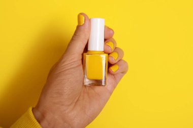 Sarı bir arka plana karşı sarı bir tırnak cilası şişesi tutuyor. Güzellik, moda ve kozmetik kavramları için mükemmel..