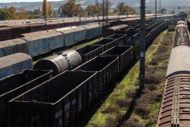 Boş, yıpranmış yük vagonları ve kargo konteynırları güneşli bir günde aşırı gelişmiş bir tren istasyonunda geniş bir manzara..