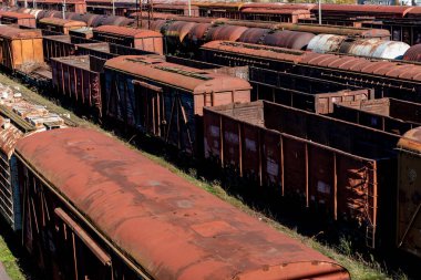 Eski, paslı yük vagonları demiryolu avlusunda aylak aylak duruyor, eskimiş metal ve zengin toprak tonlarından oluşan dokulu bir desen oluşturuyor..