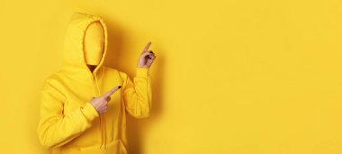 İsimsiz, sarı kapüşonlu biri boş sarı arka planı işaret ediyor. Reklam, promosyon ve yaratıcı kavramlar için ideal..