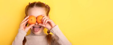 Gözlerine portakal tutarak neşeli genç bir kız, parlak sarı bir arka plana karşı komik bir surat yapıyor. Hayat dolu ve neşeli bir sağlık, eğlence ya da 