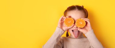 Gözlerinin üzerinde turuncu yarımlar olan gülümseyen çocuk parlak sarı arka plana karşı komik bir surat yapıyor. Sağlık, gıda ve yaşam tarzı temaları için parlak, eğlenceli bir konsept.