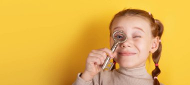 Gülümseyen kız, parlak sarı bir arka planda gözünün antika anahtarını tutuyor. Keşfi ve hayal gücünü simgeliyor..