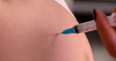 Enjeksiyon yapılan bir elin yakın çekimi, tıbbi bakım ve aşı konseptini gösteriyor.