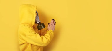 Gaz maskesi takan ve sarı kapüşonlu giyen birinin yan görünüşü, elleri birbirine bastırılmış, parlak sarı bir arka plan, boşluğu kopyala.