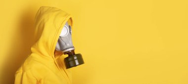 Sarı arka plana karşı gri gaz maskesi ve sarı kapüşonlu giyen kişinin yan görüntüsü, boşluğu kopyala.