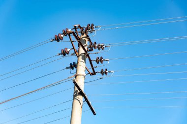 Çoklu elektrik kabloları ve yalıtımlı eski beton elektrik direği, parlak mavi gökyüzüne karşı kurulmuş. Enerji, altyapı ve iletişim kavramları için ideal.