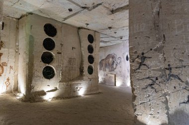 Taş duvarlı şarap mahzeni, istiflenmiş şişelerle aydınlatma, mamut mağara resimleri ve tarihi bir ortam için antik tarz graffiti içeriyor..