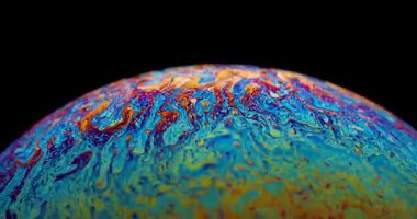 Renkli bir sabun baloncuğunun 4K yakın çekim videosu zarif bir şekilde yüzüyor, canlı, sürekli değişen renkler ve parıldayan yansımalar sergiliyor..