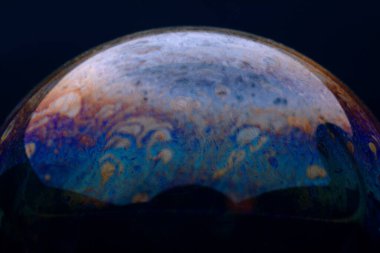 Renkli bir sabun baloncuğunun yakın çekimi, koyu bir arkaplanda hareketli girdap desenleri gösteriyor, soyut ve yaratıcı tasarımlar için mükemmel..