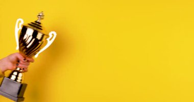 Parlak sarı bir arka planda altın kupayı tutan bir elin yakın çekimi. Zaferin, başarının, başarının ve kazanmanın sembolü. Kutlama ve ödül konsepti. İzole edilmiş, 4K video.