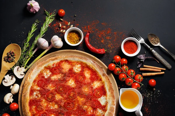Pizza italienne sur une assiette et ingrédients de cuisson : huile, tomate, poivre, épices sur fond noir — Photo