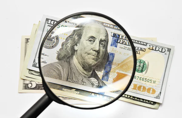 Billetes de dinero dólares en una lupa sobre un fondo blanco — Foto de Stock