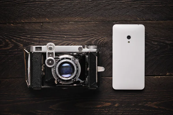 Vintage old photographic field film sing lens camera with a white smartphone on a darkness wooden background — Stock Photo, Image